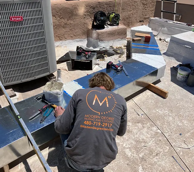 Modern Degree HVAC technician installing rooftop ductwork beside a Bryant outdoor air conditioning unit